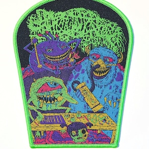 May include: A shield-shaped embroidered patch with a bright neon green border. The design features three colorful monsters in purple, blue, and green, sitting at a yellow table with various small items, set against a dark background with a green cloud.