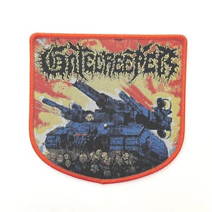 May include: A red, white, and yellow embroidered patch with the band name "Terrorizer" in black lettering. The patch features a tank with a cannon and a background of flames.