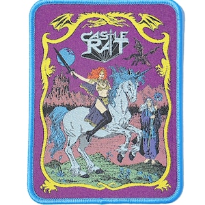 May include: A rectangular embroidered patch with a light blue border featuring a purple background. The design shows a figure with red hair riding a white unicorn, holding a sword, with a wizard standing nearby. The text CASTLE RAT is at the top.
