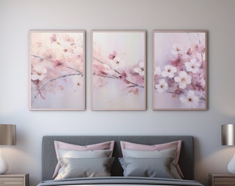 May include: A gray upholstered bed with a white duvet and three framed watercolor paintings of pink and white flowers on the wall above the headboard.