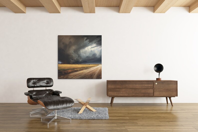 May include: A black leather armchair with a matching ottoman sits in front of a large canvas painting depicting a dramatic stormy sky over a dirt road in a field. A wooden coffee table and a wooden cabinet with a black speaker on top are also in the room.