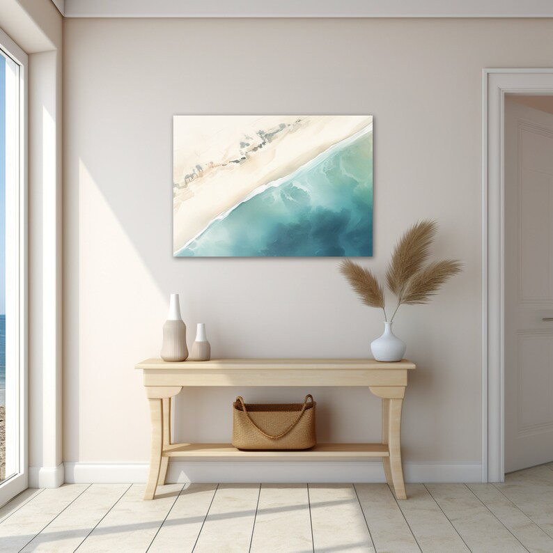 May include: A light wood console table with a woven basket on the bottom shelf. A white vase with dried pampas grass sits on the top shelf. A painting of a beach scene with blue water and white sand hangs on the wall above the table.