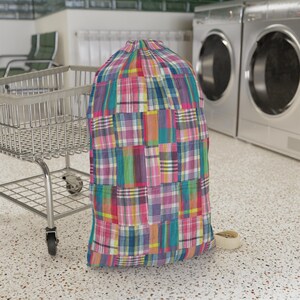 Può includere: Un sacco portabiancheria alto e cilindrico caratterizzato da un vivace motivo a quadri patchwork multicolore. Il tessuto presenta una griglia di quadrati nelle tonalità del rosa, blu, giallo, verde e bianco. Ha una chiusura a coulisse.