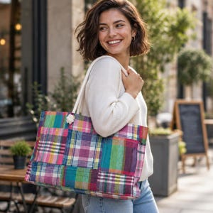 May include: A large rectangular tote bag featuring a vibrant patchwork design of multicolored plaid fabric squares in shades of pink, purple, green, and blue, equipped with thick white rope handles for carrying over the shoulder.