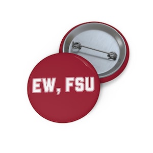 May include: A round pin-back button with a deep red surface and the white text "EW, FSU" printed in a bold, block-style font. The back of the button is metallic silver and features a standard pin mechanism for attachment to clothing or fabric items.