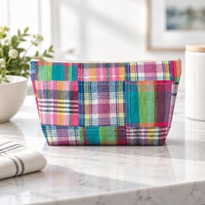 May include: A rectangular zippered pouch featuring a patchwork design of multicolored plaid fabric squares in shades of pink, teal, yellow, purple, and blue. The pouch has a structured shape with a gold-toned zipper along the top edge.