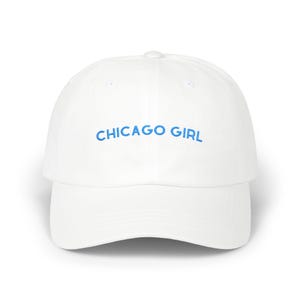 May include: A white baseball cap featuring the text CHICAGO GIRL embroidered in light blue thread across the front panel. The cap has a structured crown, a curved brim, and a button at the top center, presenting a clean and simple design.