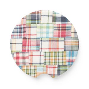 Puede incluir: Un posavasos circular para coche con un patrón de cuadros tipo patchwork multicolor. El diseño consta de varios segmentos rectangulares en tonos rojos, azules, verdes y naranjas sobre un fondo blanco, con una pequeña muesca semicircular abajo.