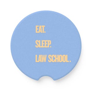 May include: A round, light blue car coaster with a textured surface and a small semi-circular notch at the bottom edge. The text EAT. SLEEP. LAW SCHOOL. is printed in a bold, light yellow sans-serif font across the center of the coaster.