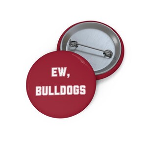 Könnte beinhalten: Ein runder Ansteckbutton mit dunkelrotem Hintergrund und weißem Text, der EW, BULLDOGS lautet. Die Rückseite des Buttons besteht aus silberfarbenem Metall und verfügt über eine horizontale Nadel zum Befestigen an Kleidung.