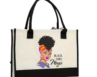 May include: A white canvas tote bag with black handles and a black bottom. The bag features a colorful illustration of a woman with an afro and the text "Black Girl Magic".