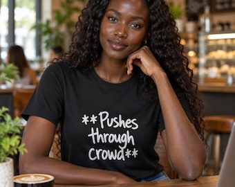 Può includere: Una t-shirt nera a maniche corte con testo bianco stampato sul davanti che recita **Pushes through crowd**. La maglia presenta uno scollo rotondo e una vestibilità standard, realizzata in tessuto nero tinta unita con scritte bianche.