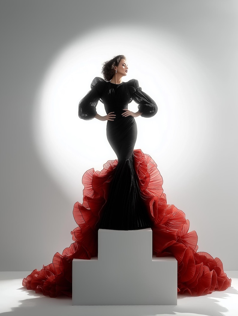 May include: A black gown with voluminous sleeves and a fitted silhouette. The gown features a dramatic red ruffled train. The model is standing on a white platform against a bright, white background.