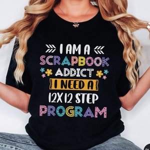May include: Black t-shirt with the text "I am a scrapbook addict I need a 12x12 step program" in colorful letters with flowers.