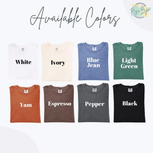 May include: A display of eight t-shirts in various colors: white, ivory, blue jean, light green, yam, espresso, pepper, and black. The text "Available Colors" is at the top, with each shirt labeled with its color name. The shirts are neatly arranged.