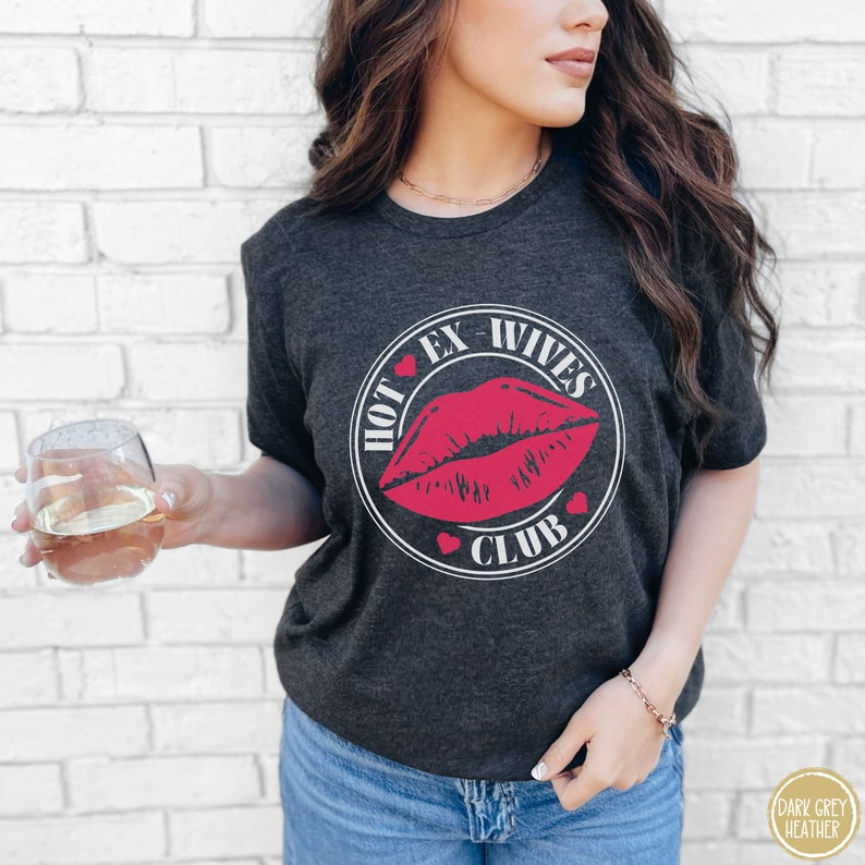 May include: A dark grey heather t-shirt with a white circle graphic featuring a red lip print and the text "HOT EX-WIVES CLUB".