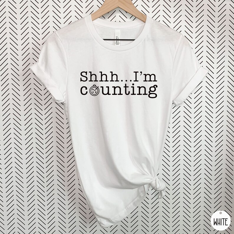 May include: White t-shirt with black text that reads "Shhh... I'm counting" and a small clock icon.