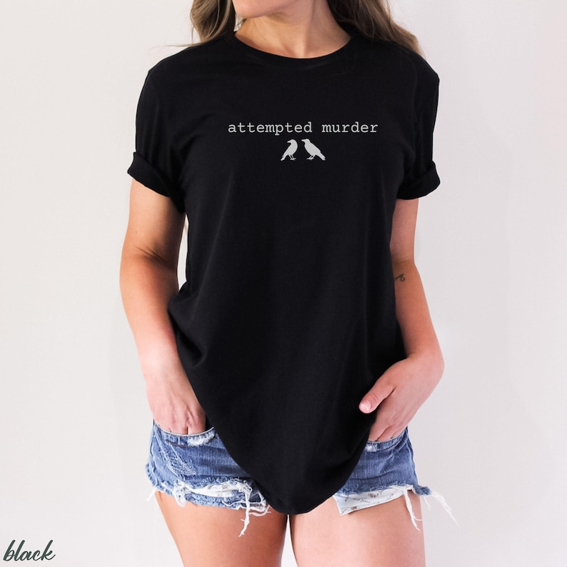 Pu&ograve; includere: T-shirt nero con la scritta "attempted murder" sopra due piccole illustrazioni di uccelli. La maglietta &egrave; a girocollo e viene indossata con pantaloncini di jeans.