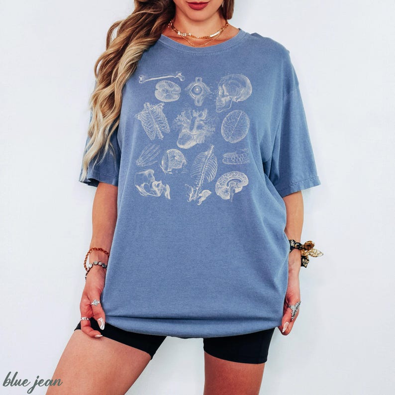 May include: A blue t-shirt with a cream-coloured anatomical illustration of human organs and bones. The design includes the brain, heart, and skull. The shirt is a relaxed fit. The words "blue jean" are at the bottom left.