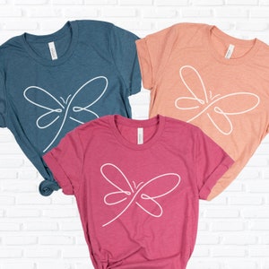 May include: Three t-shirts with a simple line drawing of a butterfly on the front. The shirts are teal, peach, and pink.