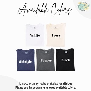 May include: A display of t-shirts in various colors: white, ivory, midnight blue, pepper gray, and black. The text "Available Colors" is at the top, with the color names printed on each shirt. The bottom text reads "Some colors may not be available for all sizes."