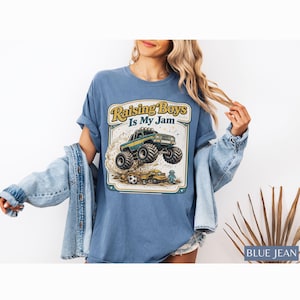May include: Blue jean t-shirt with a graphic that says "Raising Boys Is My Jam." The graphic features a monster truck, a soccer ball, and a small toy truck. The shirt is a light blue color.