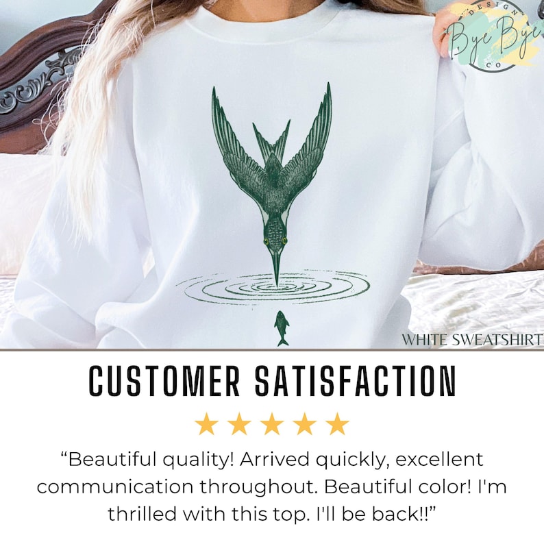 May include: White sweatshirt featuring a green illustration of a bird diving into water, with a fish below. The text "WHITE SWEATSHIRT" is at the bottom. The words "CUSTOMER SATISFACTION" are displayed with five gold stars.