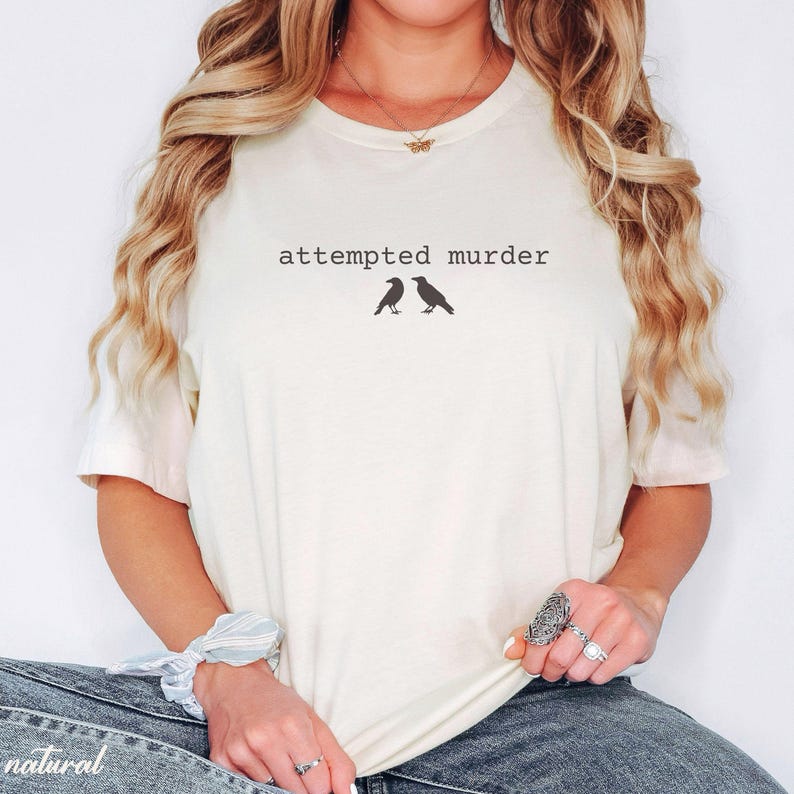Pu&ograve; includere: T-shirt color crema con la scritta "attempted murder" sopra due sagome di uccelli neri. La maglietta ha maniche corte e una vestibilit&agrave; ampia, adatta per l'uso quotidiano.