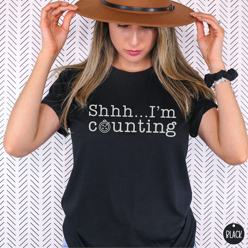 May include: Black t-shirt with white text that reads "Shhh... I'm counting" and a small stopwatch icon.