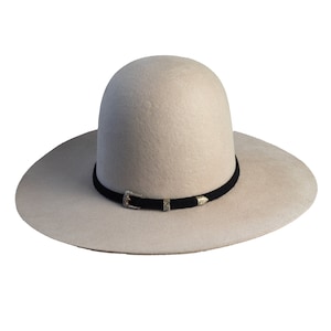 Peut inclure: Un chapeau de cowboy en feutre beige clair avec un bandeau en cuir noir et une boucle argentée. Le chapeau a une large bordure et une couronne haute.