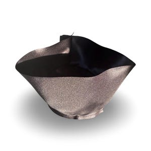 Pode incluir: Uma fita de cetim preta e prateada é dobrada em forma de cone, criando uma tigela decorativa.