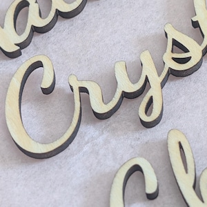 Puede incluir: Letras de madera cortadas con l&aacute;ser que forman la palabra Crystal en una fuente cursiva. Las letras tienen un acabado de madera natural clara en la parte frontal con bordes oscuros y quemados por el corte, creando un marcado contraste.
