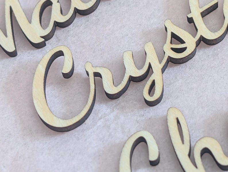 Puede incluir: Letras de madera cortadas con l&aacute;ser que forman la palabra Crystal en una fuente cursiva. Las letras tienen un acabado de madera natural clara en la parte frontal con bordes oscuros y quemados por el corte, creando un marcado contraste.