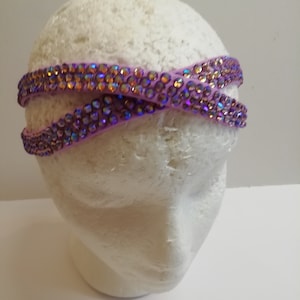 May include: A purple headband with iridescent rhinestones. The headband is on a white mannequin head.