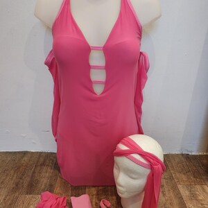 Könnte beinhalten: Ein leuchtend pinkfarbenes Kostümset, bestehend aus einem Neckholder-Top-Kleid mit Ausschnitten, einem Choker, Armdrapierungen, einem Stirnband, einer Handgelenkmanschette und einer Knöchelmanschette, präsentiert auf einer Schaufensterpuppe und einem Styroporkopf.