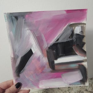 May include: Abstract painting on canvas with bold brushstrokes. The artwork features a vibrant mix of colors, including pink, black, gray, and white. The composition is dynamic, with a sense of movement and texture. The painting is held by a hand.
