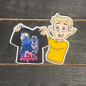 May include: A black t-shirt with a colorful graphic of a wolf howling at the moon. A cartoon character with blonde hair and a yellow shirt is holding the t-shirt.