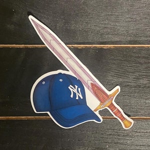 May include: A blue baseball cap with a white "NY" logo is paired with a pink and gold sword. The sword has a red handle and a gold blade with a white inscription.