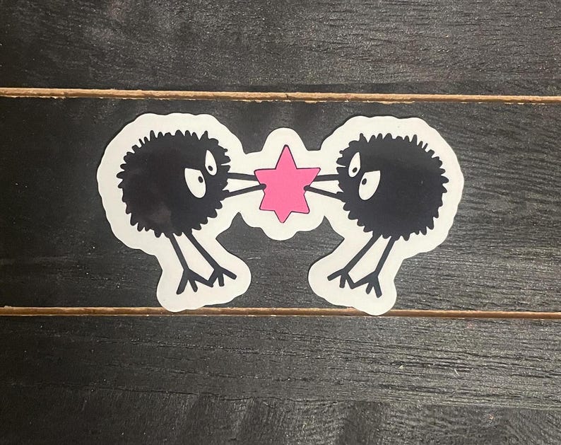 May include: Two black fuzzy creatures with large eyes are holding a pink star. The creatures are facing each other and have a playful expression.