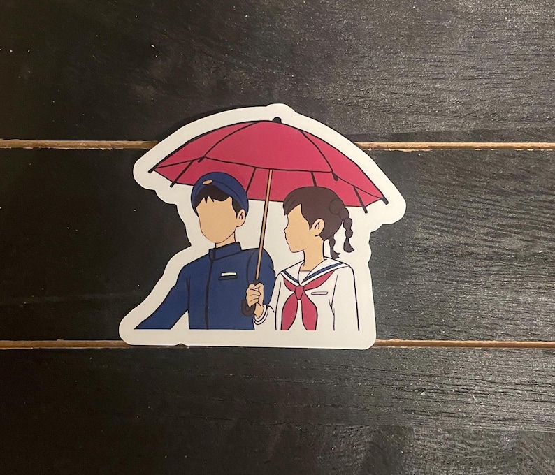 May include: A sticker featuring a cartoon illustration of a boy and girl walking under a red umbrella. The boy is wearing a blue uniform and the girl is wearing a white uniform with a red ribbon.