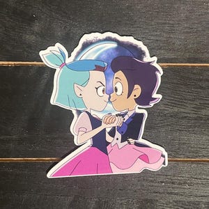 May include: A sticker featuring two cartoon characters, a girl with blue hair and a boy with purple hair, dancing together in front of a blue and purple moon. The girl is wearing a pink dress and the boy is wearing a black suit.