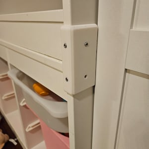 May include: White wooden storage unit with shelves and drawers. The unit has a white plastic trim piece on the side, secured with screws.