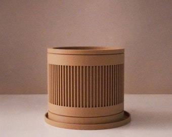 May include: A light brown cylindrical planter with a decorative slatted design. The planter has a matching saucer.