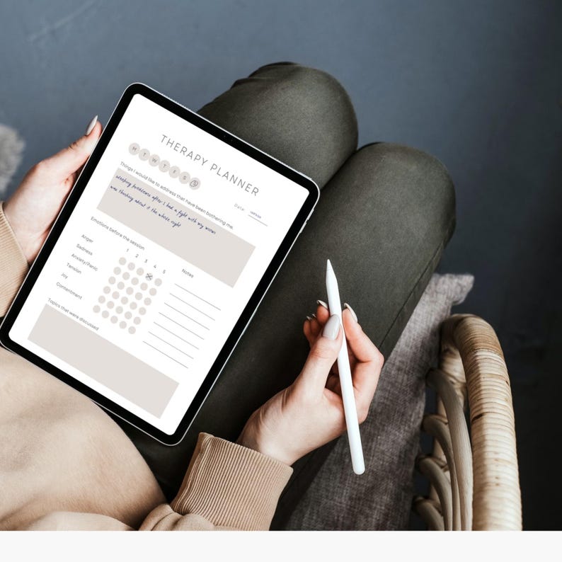 May include: A digital tablet with a white background and the text "Therapy Planner" at the top. The tablet has a calendar and a section for notes. A person is holding the tablet and a white stylus.