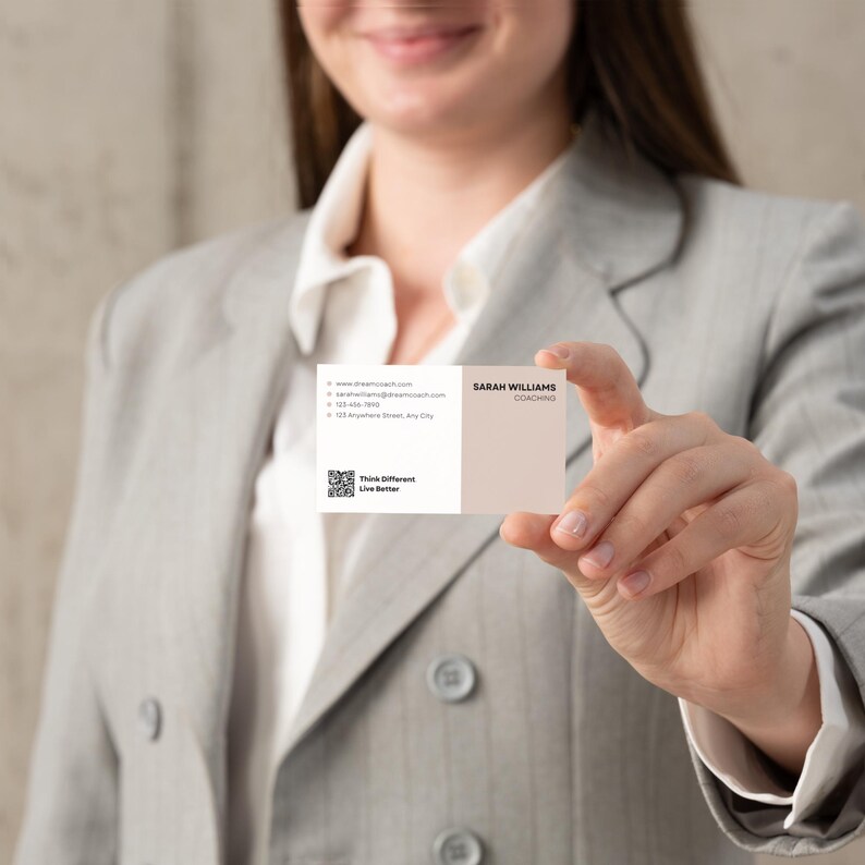 May include: A business card held by a person, featuring a two-tone design in white and beige. The card displays the name "Sarah Williams" and the word "Coaching." Additional text includes contact information and the phrase "Think Different, Live Better."