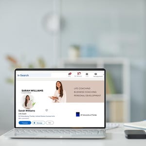 May include: A laptop displays a professional profile page. The profile belongs to Sarah Williams, a life coach. The page highlights "Life Coaching," "Business Coaching," and "Personal Development." The laptop is on a white desk with a notebook and a black device.