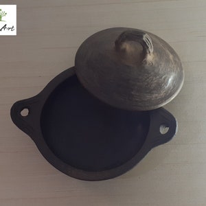 Puede incluir: Una olla de cerámica marrón oscuro hecha a mano con una tapa a juego. La olla tiene una forma redondeada con dos asas y un asa texturizada en la tapa. El logotipo de Ali Art está en la esquina superior izquierda.