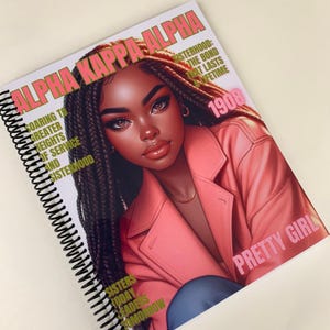 May include: A pink and gold spiral bound notebook with a black and white illustration of a woman with braids. The notebook cover features the text "ALPHA KAPPA ALPHA" and "PRETTY GIRL".
