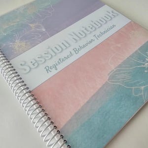 May include: A spiral-bound notebook with a white cover featuring horizontal bands of pastel purple, pink, and blue with white floral line art. The text Session Notebook Registered Behavior Technician is printed in white across the center band.