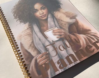 May include: A spiral bound planner with a brown and white illustration of a person holding a cup of coffee. The text "Faith Planner" is printed in gold on the cover.